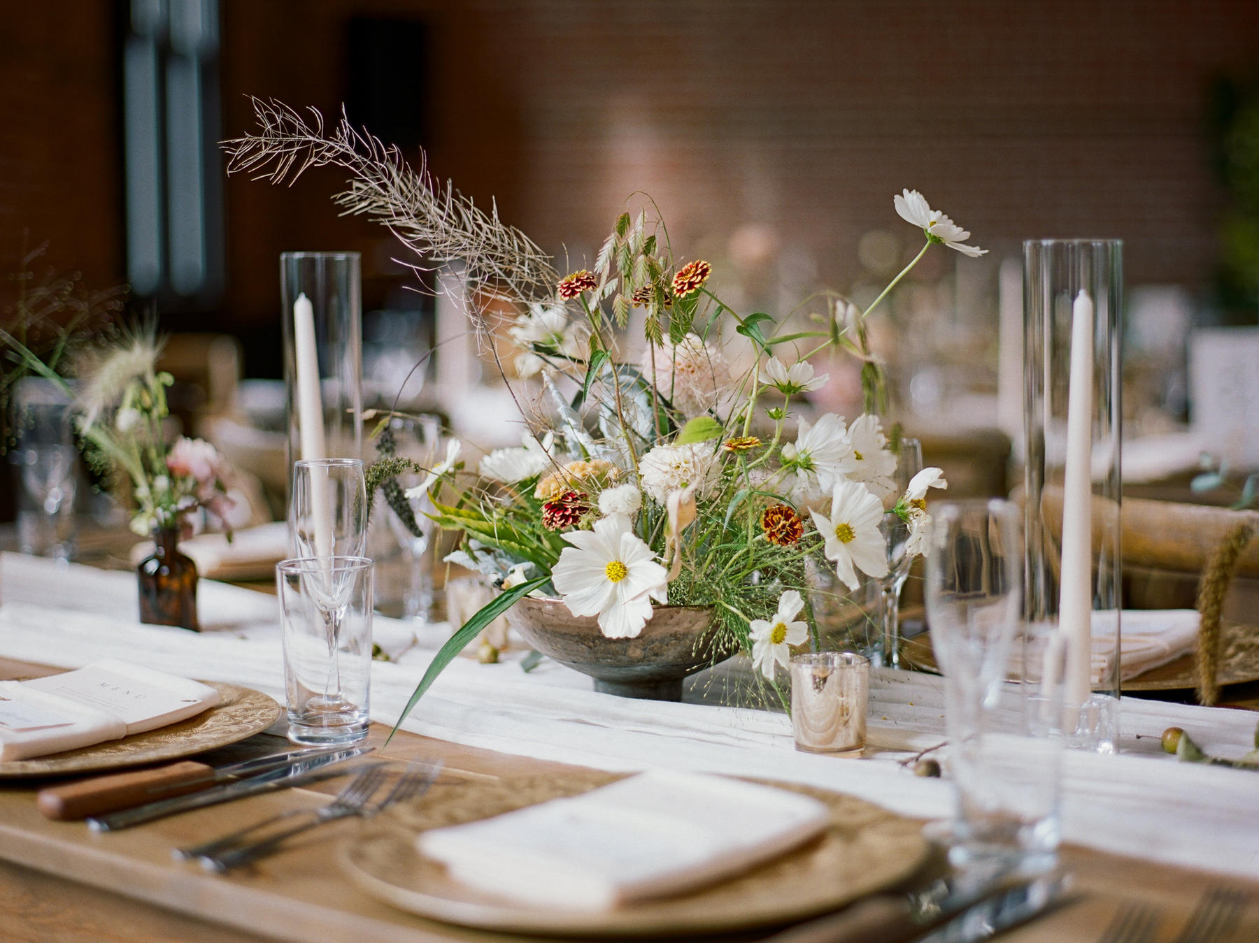 Seasonal centerpiece of cosmos, zinnias and grasses on a candlelit table